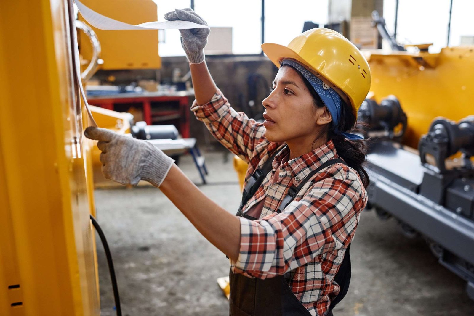 Young Hispanic woman in coveralls and safety helmet looking at working plan